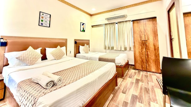 Une chambre d’hôtel avec deux lits, un ventilateur de plafond, un appareil de climatisation et une armoire en bois.