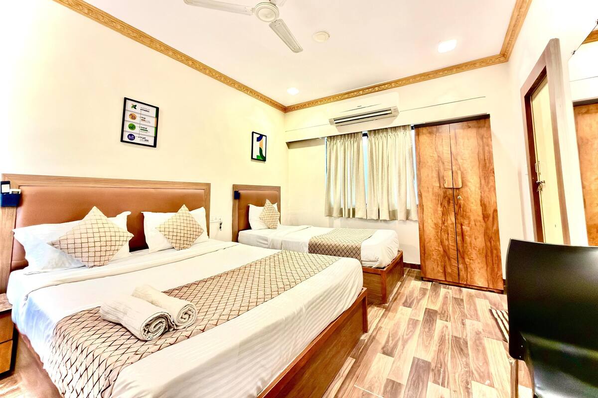 A hotel room with two beds, a ceiling fan, an air conditioning unit, and a wooden wardrobe.