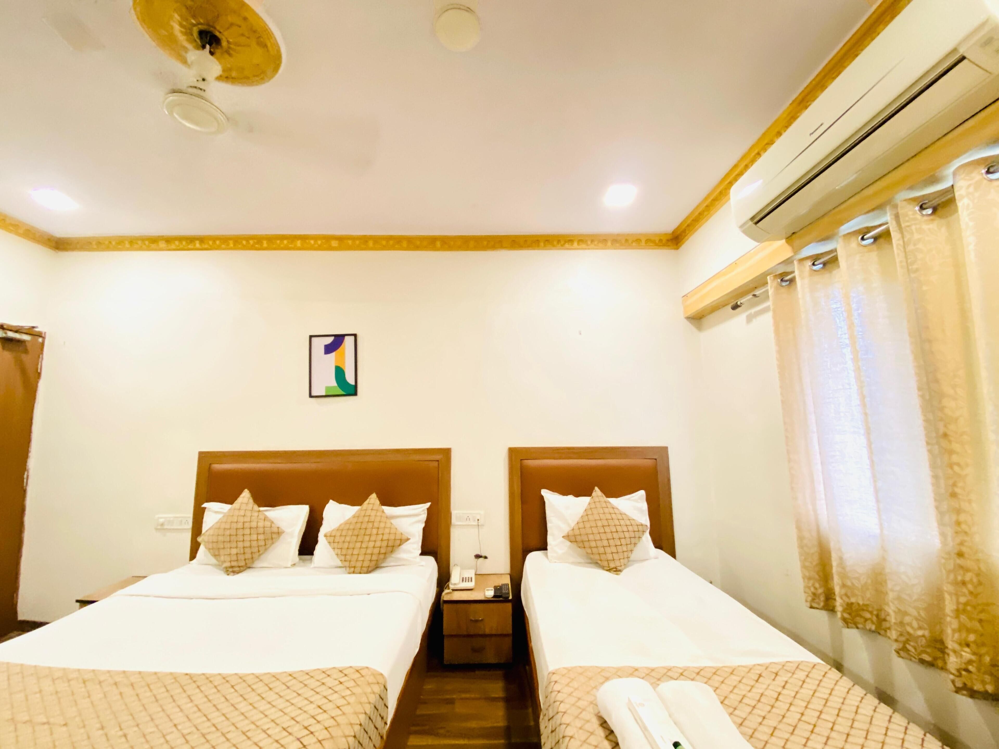 A hotel room with two beds, a ceiling fan, an air conditioning unit, and a single nightstand with a phone and a lamp.