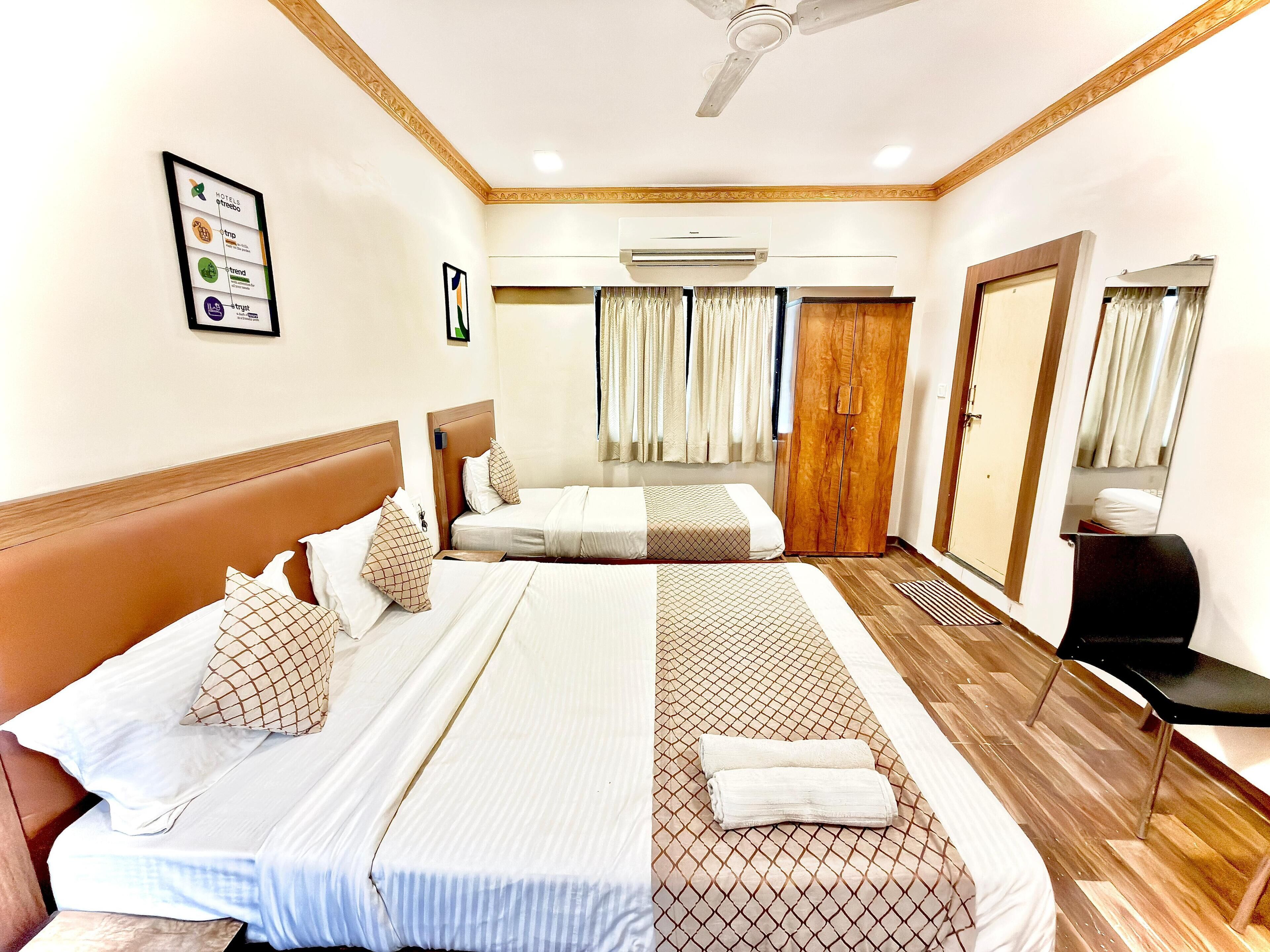 Habitación de hotel con dos camas, ventilador de techo, unidad de aire acondicionado y armario de madera.