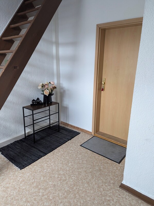 A hallway with a wooden door, a black metal console table with a vase of flowers, a black rug, and a small mat.