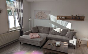 A modern living room with a grey sectional sofa, a small round coffee table, and a wooden shelf with decorative items. - Apartment "Harzbahnblick" (Wernigerode)