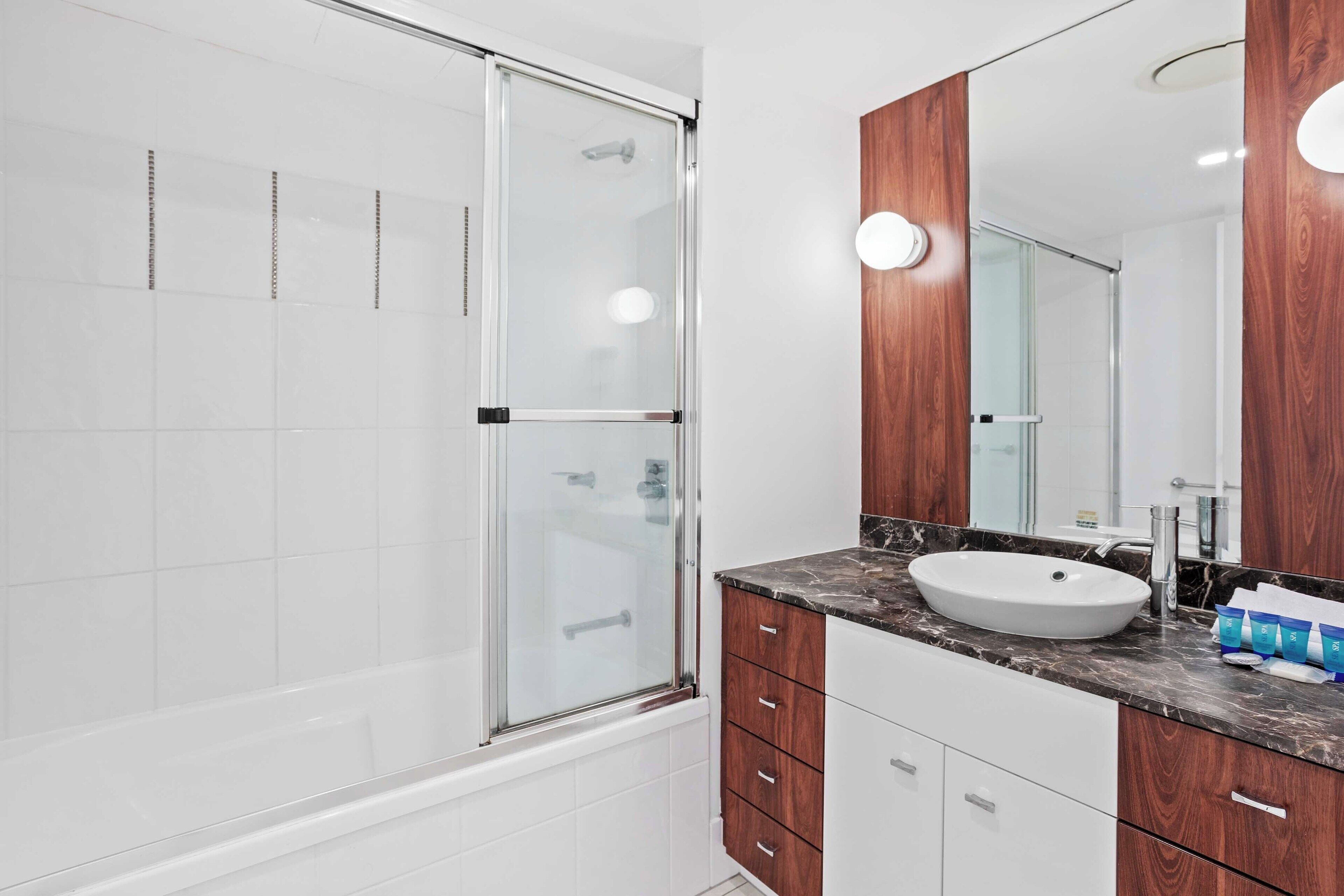 A modern bathroom with a glass shower enclosure, a white sink, wooden cabinets, and a large mirror.