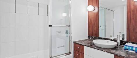 A modern bathroom with a glass shower enclosure, a white sink, wooden cabinets, and a large mirror.