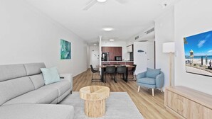 A modern living room with a grey sofa, a round wooden coffee table, and a blue armchair. A dining area with a wooden table and chairs is visible in the background. - 12th Floor Ocean Views in Chevron Towers (Surfers Paradise)
