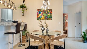 Un comedor moderno con una mesa redonda de vidrio, cuatro sillas de mimbre y una base central de madera similar a un tronco.