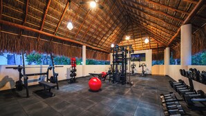 Un gimnasio con techo de paja, varios equipos de ejercicio y una pelota roja grande.