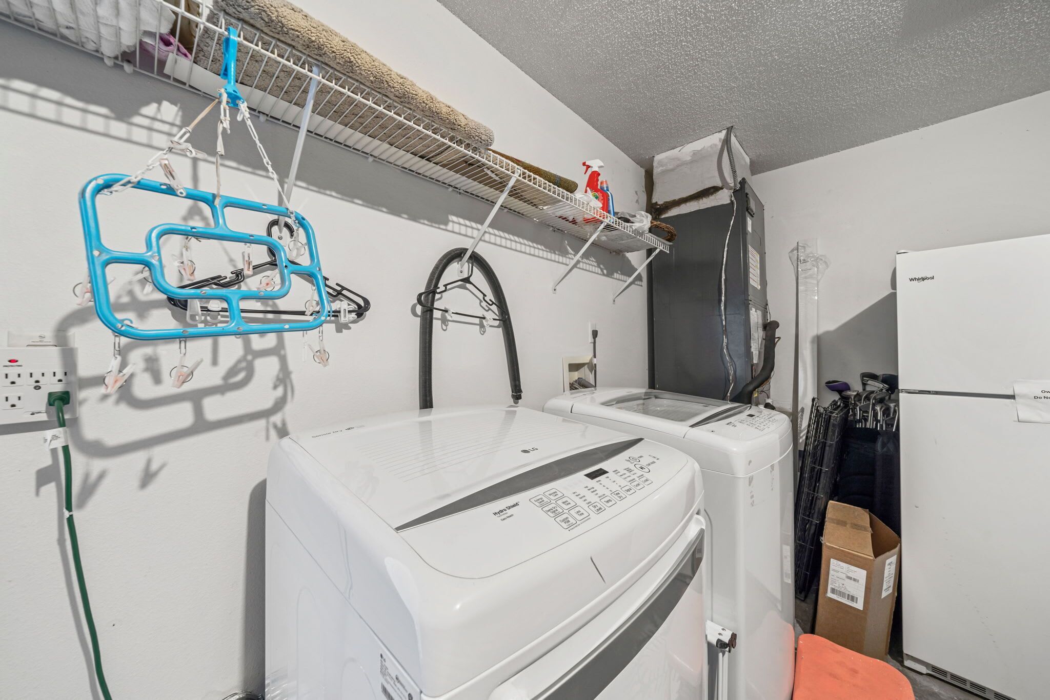 Een wasruimte met een wasmachine, droger en een plank met schoonmaakmiddelen.