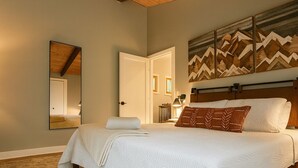 Un dormitorio con una cama grande, techo de madera, un espejo y una obra de arte con temática de montaña en la pared.