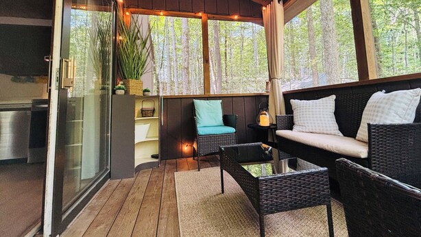 Un área de estar al aire libre acogedora, con mobiliario de mimbre, una puerta de cristal que da a la cocina y vistas a un bosque.