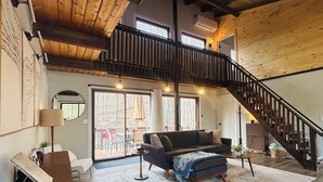 Un amplio salón con techo de madera, una escalera y un gran ventanal con vistas a una terraza.