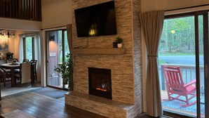 Un amplio espacio de estar con chimenea de piedra, un televisor de pantalla plana y un gran ventanal corredizo que da a una terraza exterior.