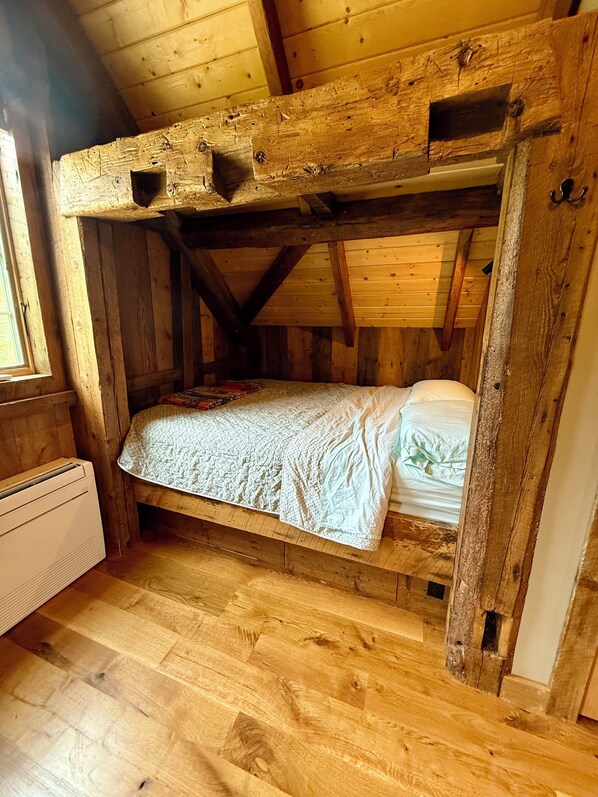 A rustic wooden bunk bed with a patterned bedspread and pillows, a radiator, and wooden flooring.