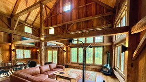 Un interior de cabaña espacioso con un amplio sofá de cuero, vigas de madera y grandes ventanales.