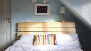 A bedroom with a wooden headboard, a white bedspread, a colorful striped pillow, a framed picture on the wall, and a bedside lamp. - Cozy Flat in Villa Near Old Town (București)