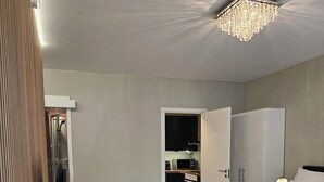 A bedroom with a bed, a dresser, a TV on a stand, a wardrobe, and a microwave in the kitchen area. - Cozy & Central studio in the royal heart of Oslo (Oslo)
