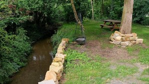 Un mur de pierres le long d’une rivière, une table de pique-nique et une balançoire dans un espace boisé.