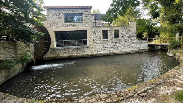 Un bâtiment en pierre agrémenté d’un élément décoratif aquatique, d’un pont en bois et d’un petit quai.