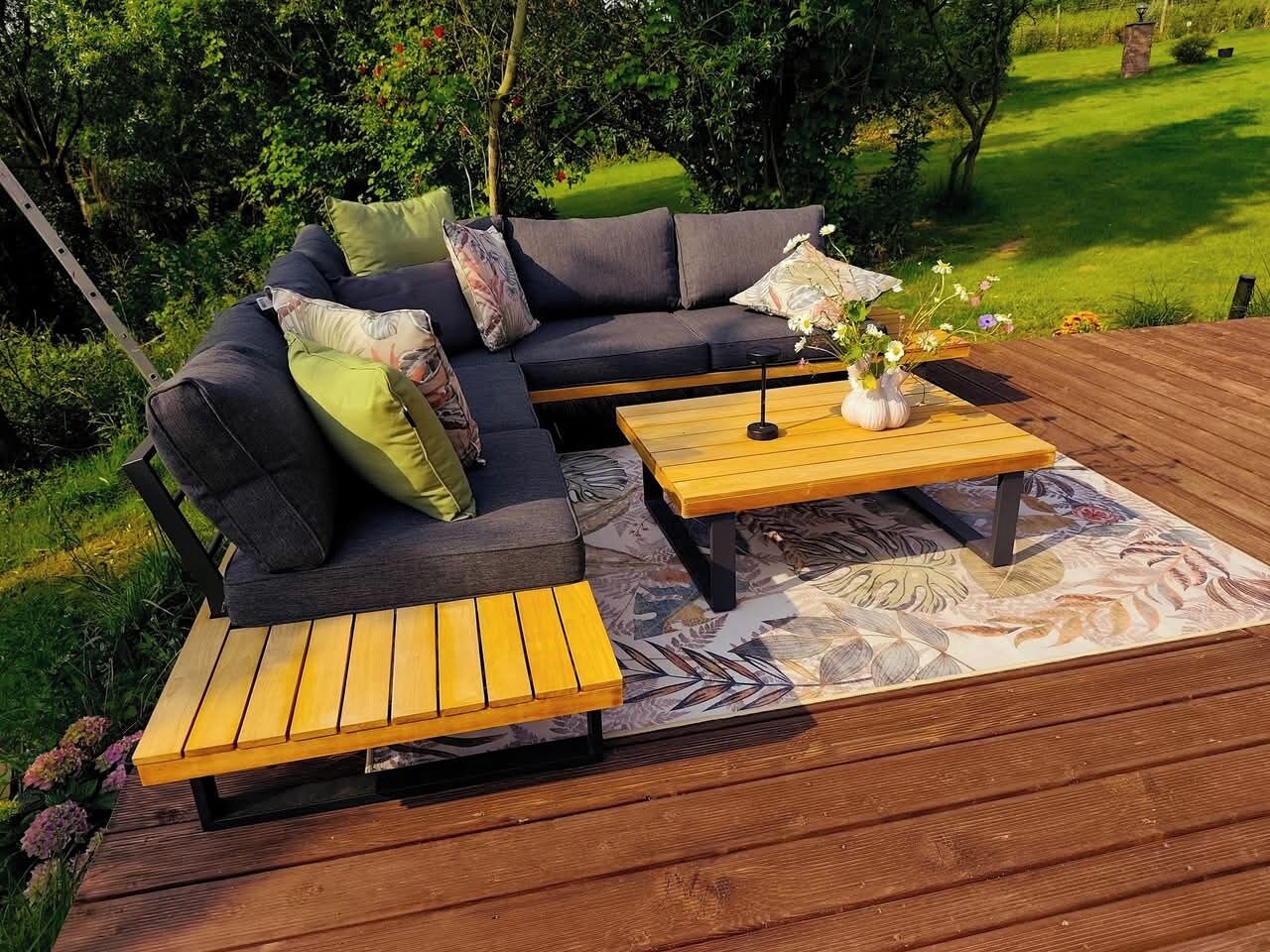 En træterrasse med en mørk sofa og to træborde.
