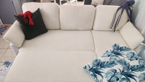 Een witte bank met een zwart en blauw bloemenkussen, een witte plaid en een blauw versierd vloerkleed.