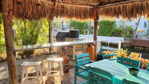 Een terras buiten met rieten dak, houten terras en zitplaatsen.