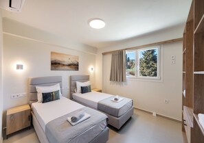 Habitación de hotel con dos camas, un cuadro, una ventana con cortinas y vistas a árboles.