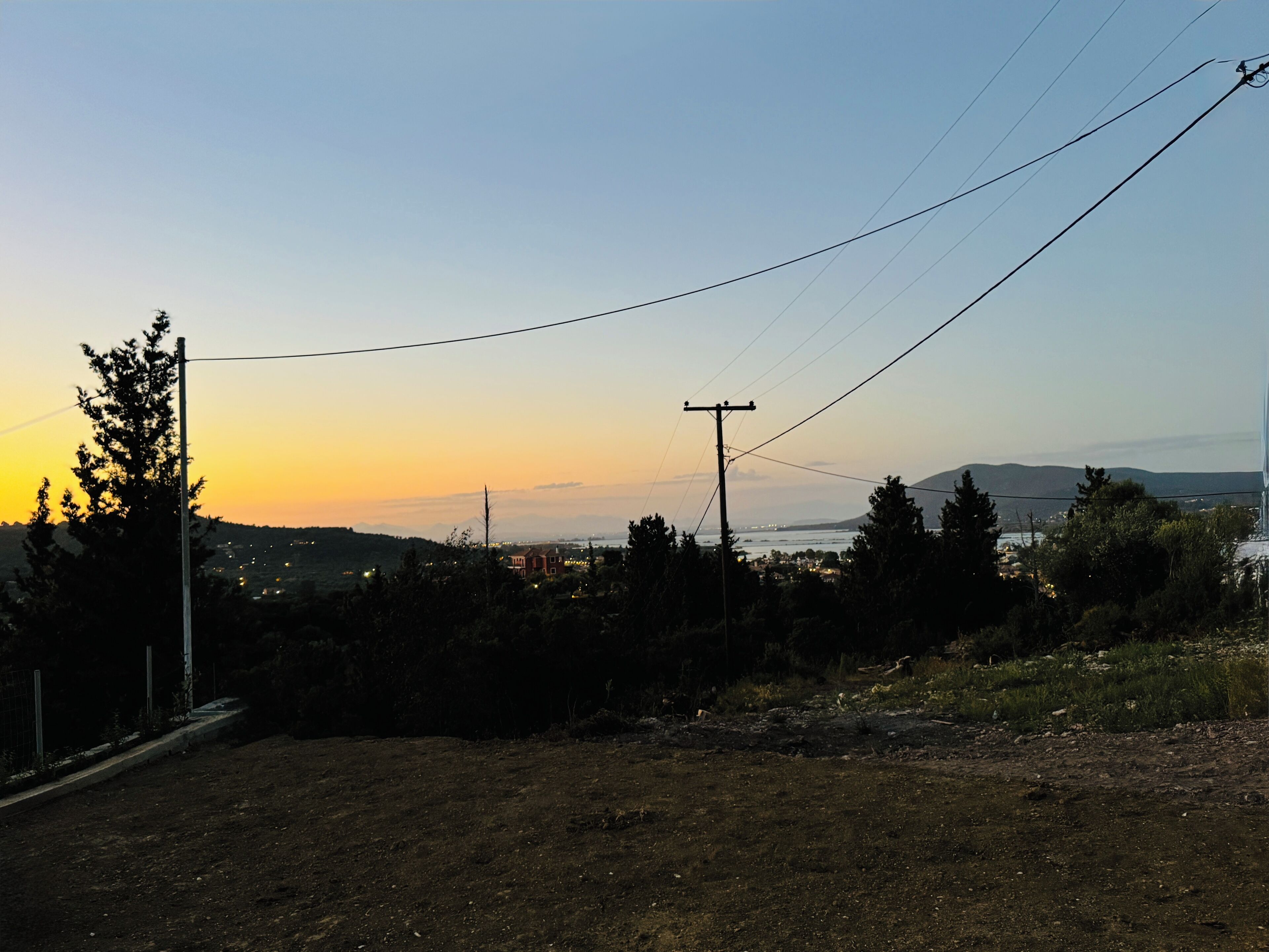 A rural landscape with a dirt road, power lines, and a distant view of a town and mountains.