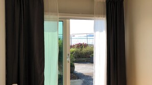Ein Zimmer mit einem Bett, einem Fenster mit schwarzen Vorhängen und Blick auf einen Garten.