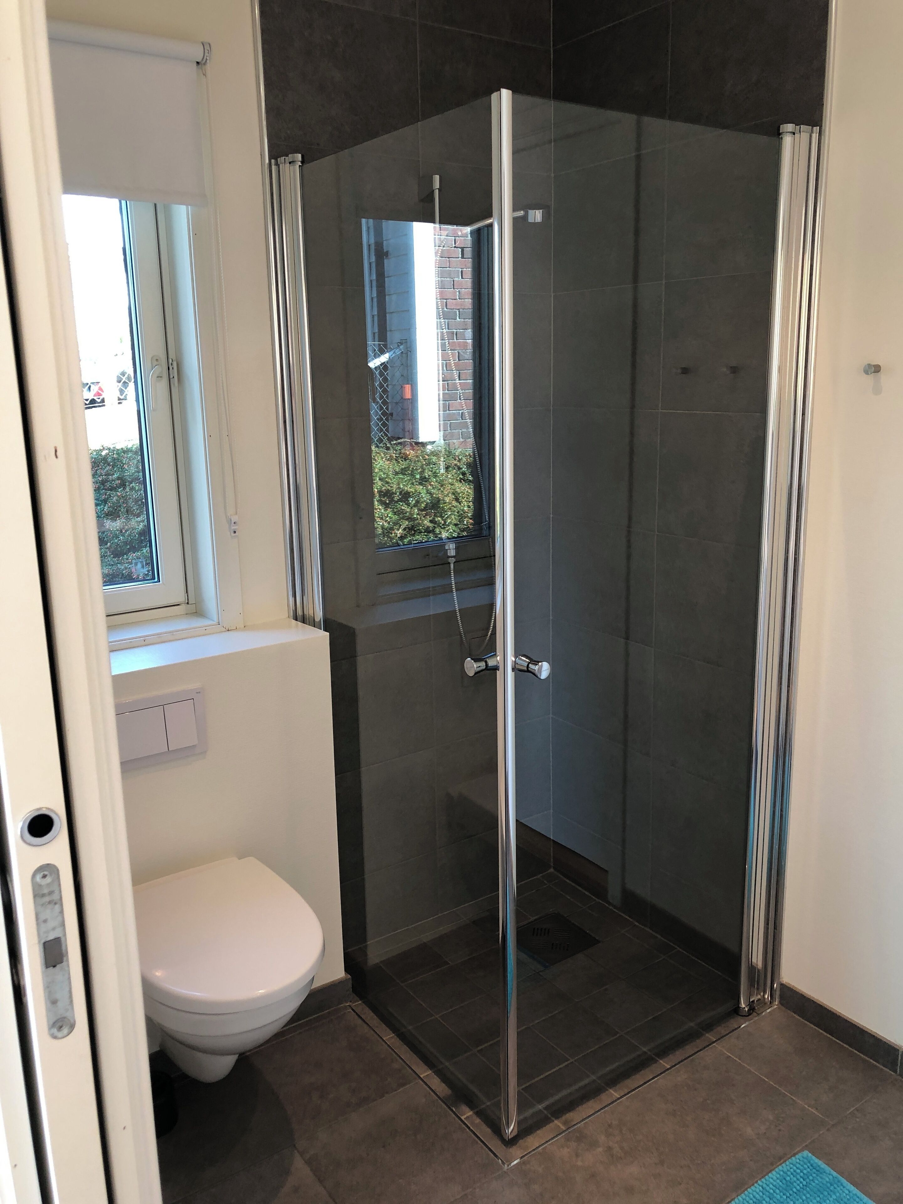 Ein modernes Badezimmer mit einer Duschkabine aus Glas, einer Toilette und einem Fenster.