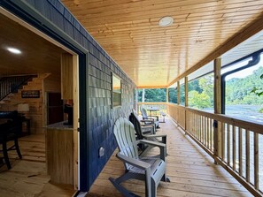 Een houten terras met Adirondack-stoelen, een trap naar een hoger niveau en uitzicht op een rivier.