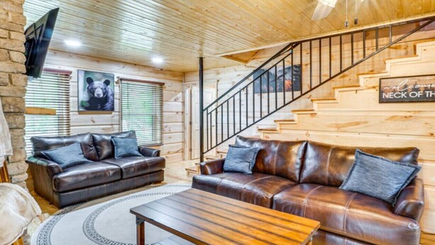 Ein gemütliches Blockhaus-Interieur mit Holzbalkendecke, einer Ledersofa, einem Couchtisch und einer Treppe.