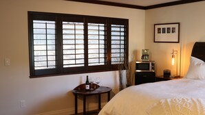 A hotel room with a large bed, a small table with a bottle and glasses, a microwave, a lamp, and a window with blinds. - High-End Private Suite with Deck & Mountain Views in Prime Marin County Location (Novato)