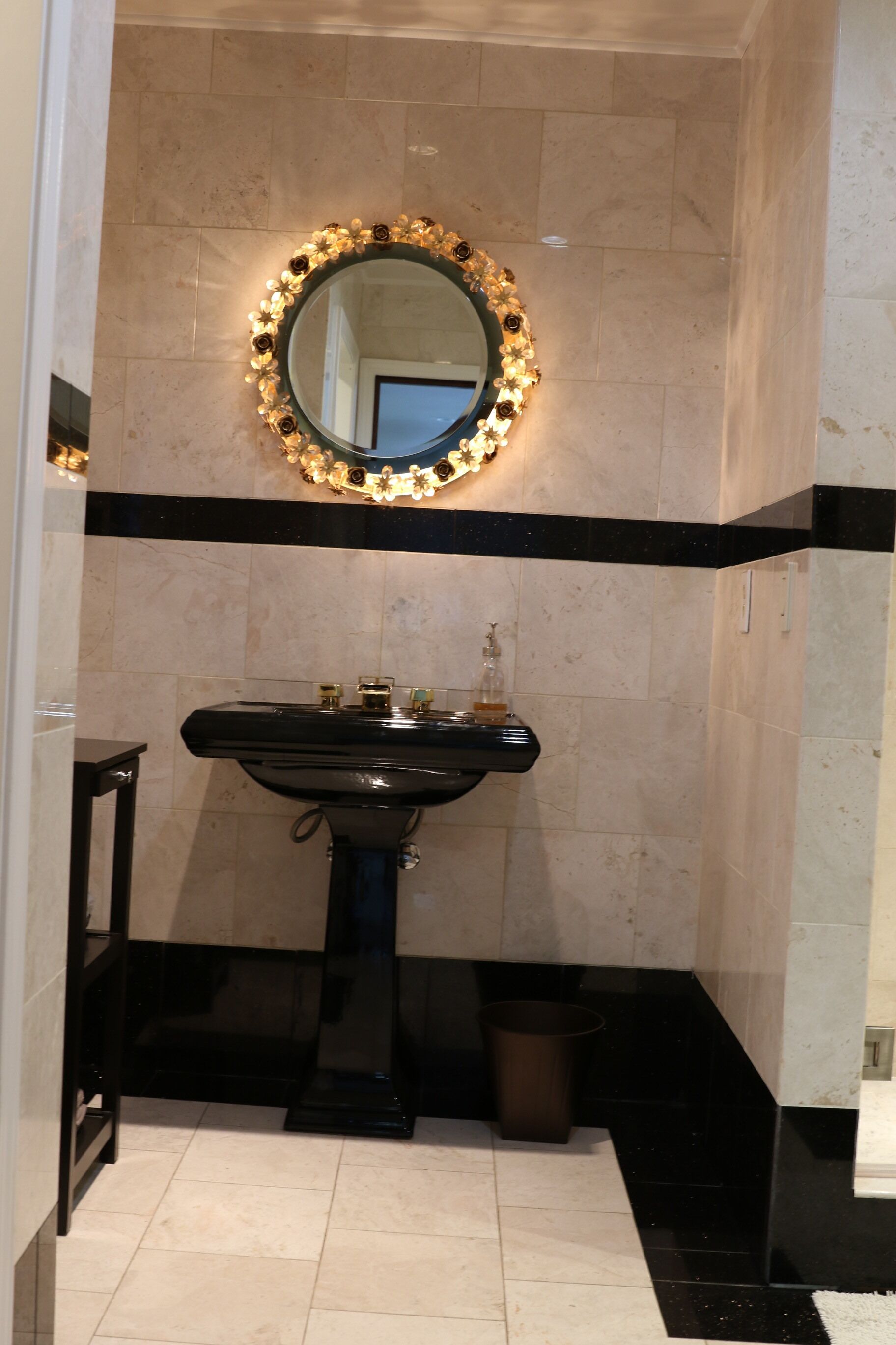 A bathroom with a black sink, a mirror with a floral frame, and a trash bin.