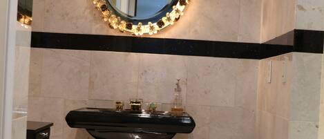 A bathroom with a black sink, a mirror with a floral frame, and a trash bin.