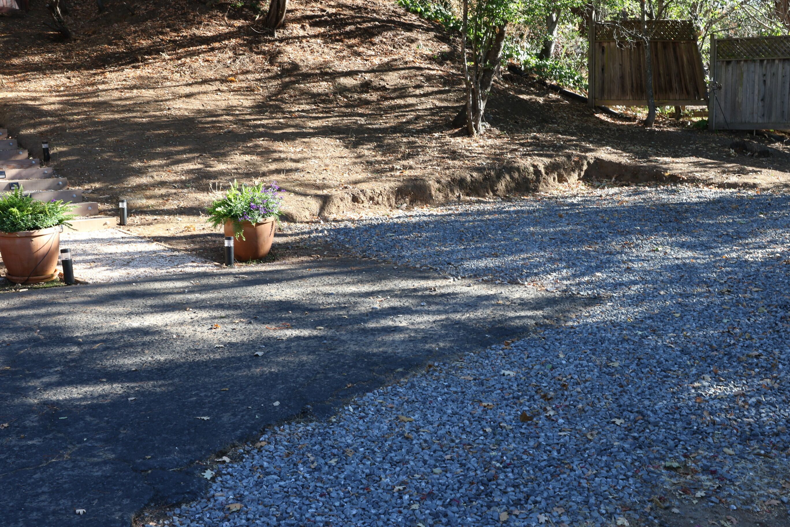 A gravel driveway leading to a wooden fence, with potted plants on either side.