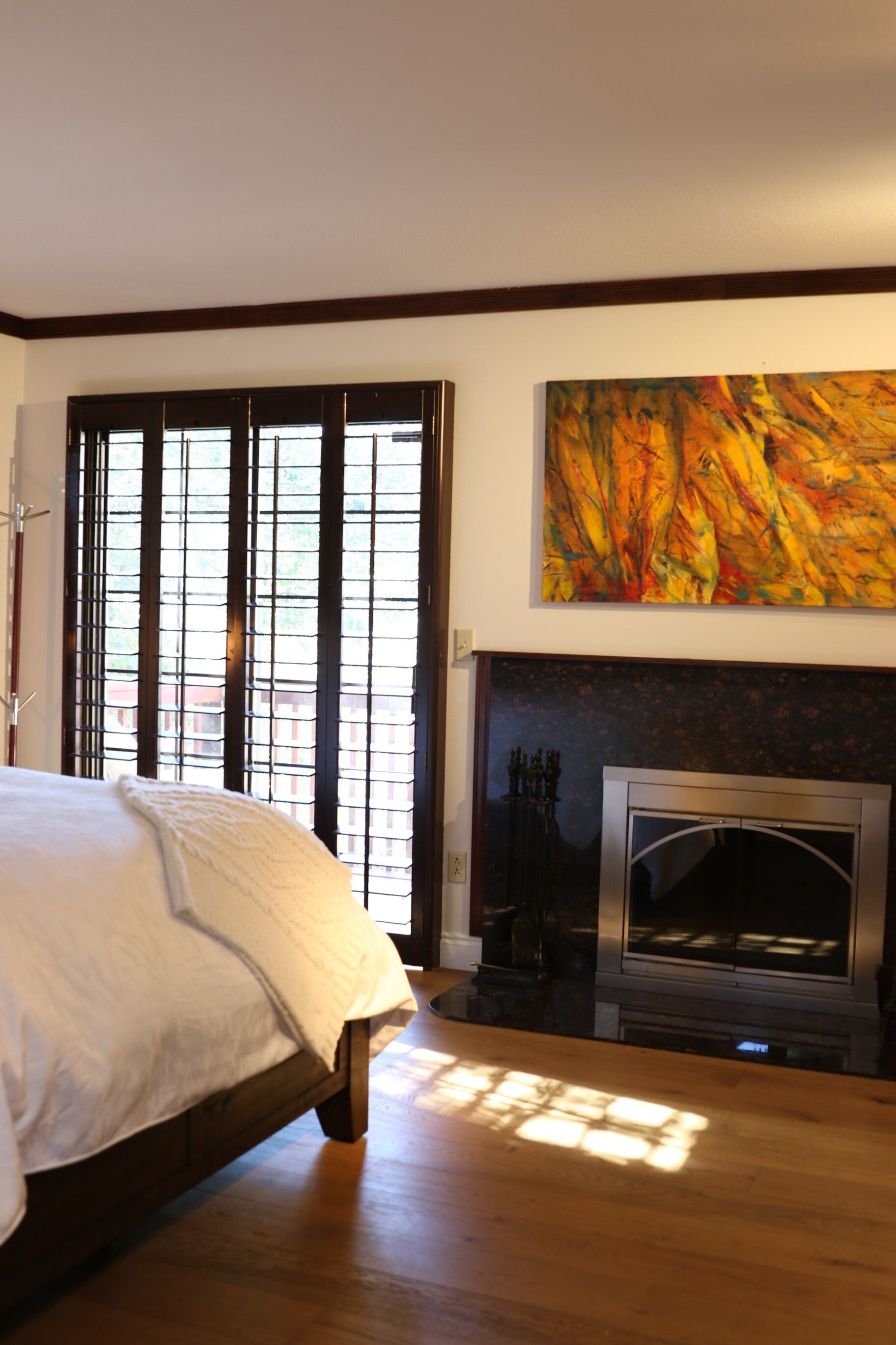 A bedroom with a bed, a fireplace, and a large abstract painting on the wall.