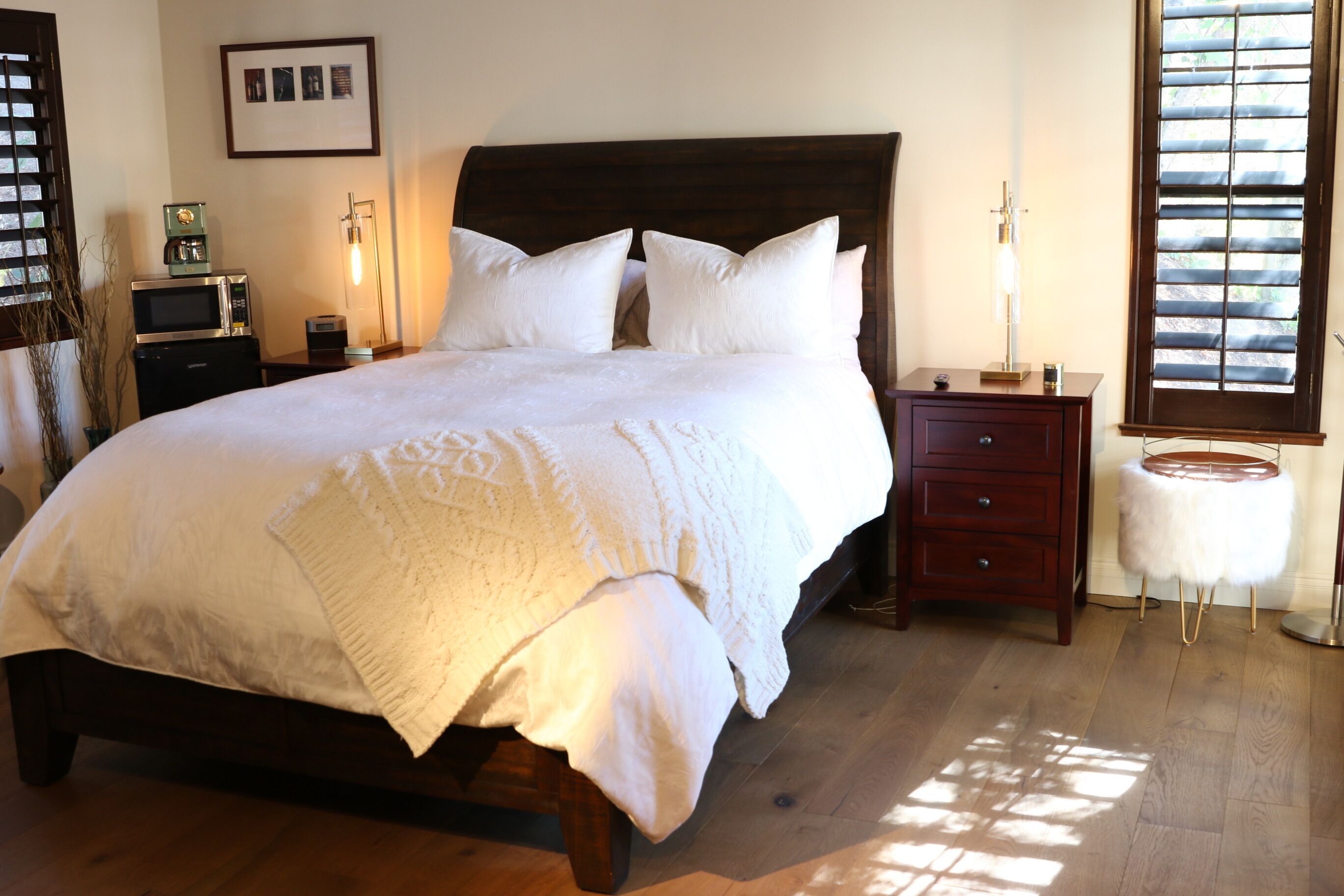 Un dormitorio ordenado con una cama grande, mesitas de noche, una lámpara y un taburete pequeño.