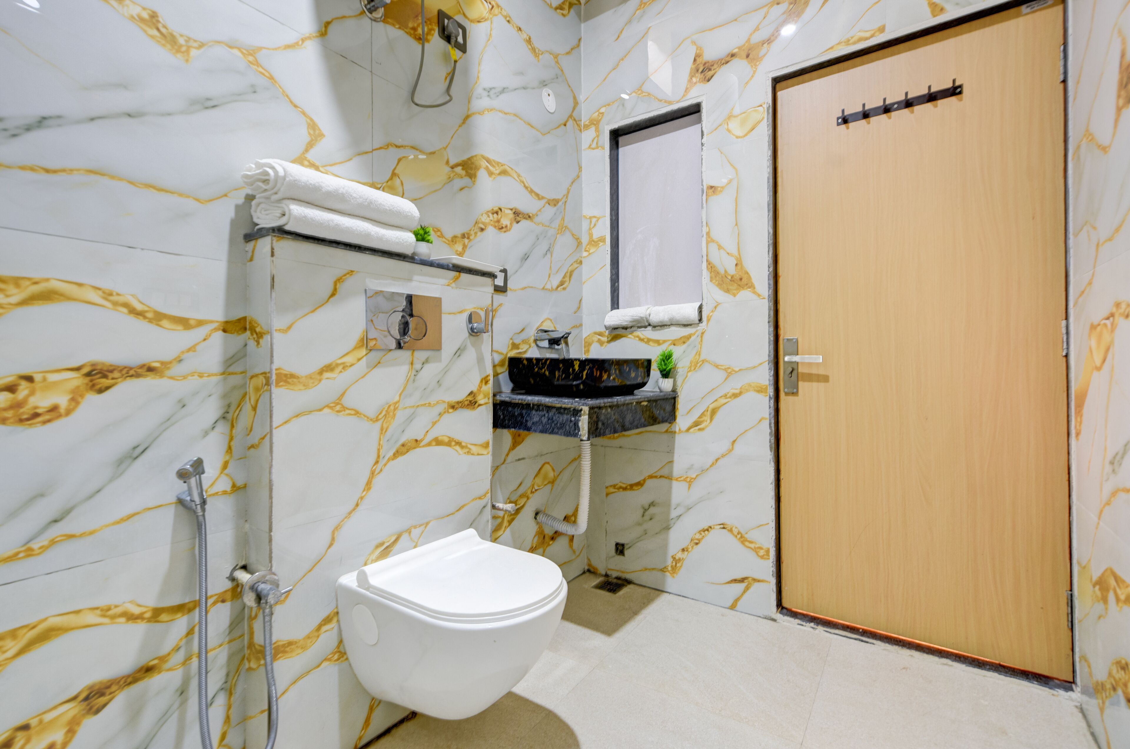 A bathroom with a marble wall, a toilet, a sink with a mirror, and a wooden door.