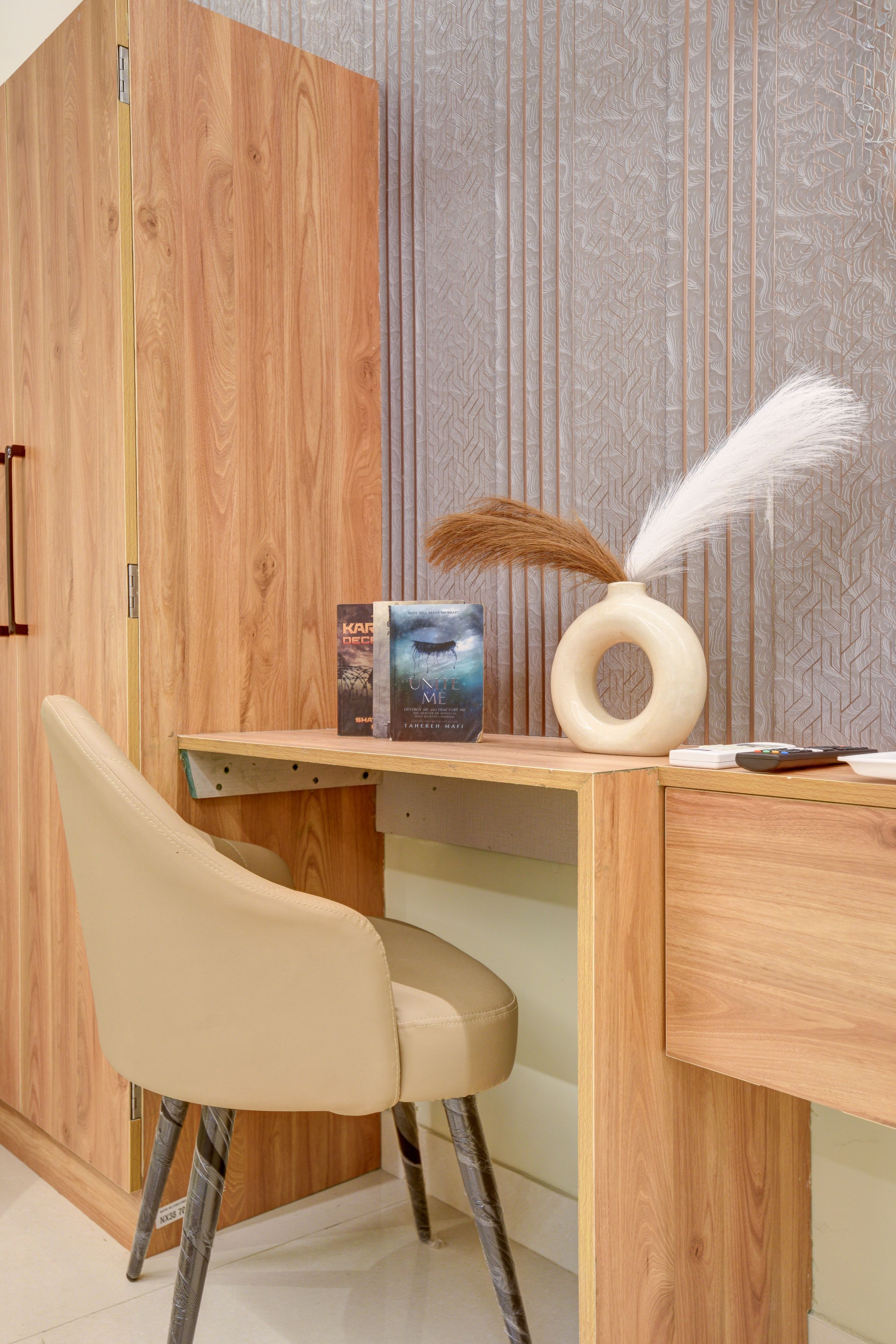 A wooden desk with a chair, a vase with feathers, and books.