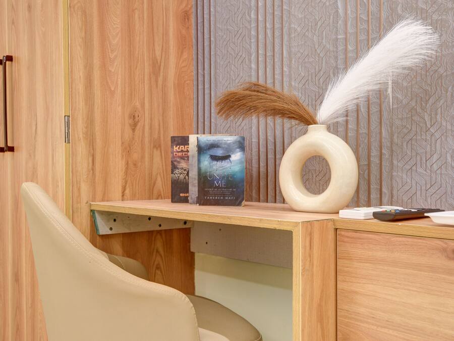 A wooden desk with a chair, a vase with feathers, and books.