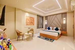 A modern hotel room with a large bed, a small round table, two chairs, a ceiling fan, and a large artwork on the wall. - HOTEL AERO HOMESTAY (New Delhi)