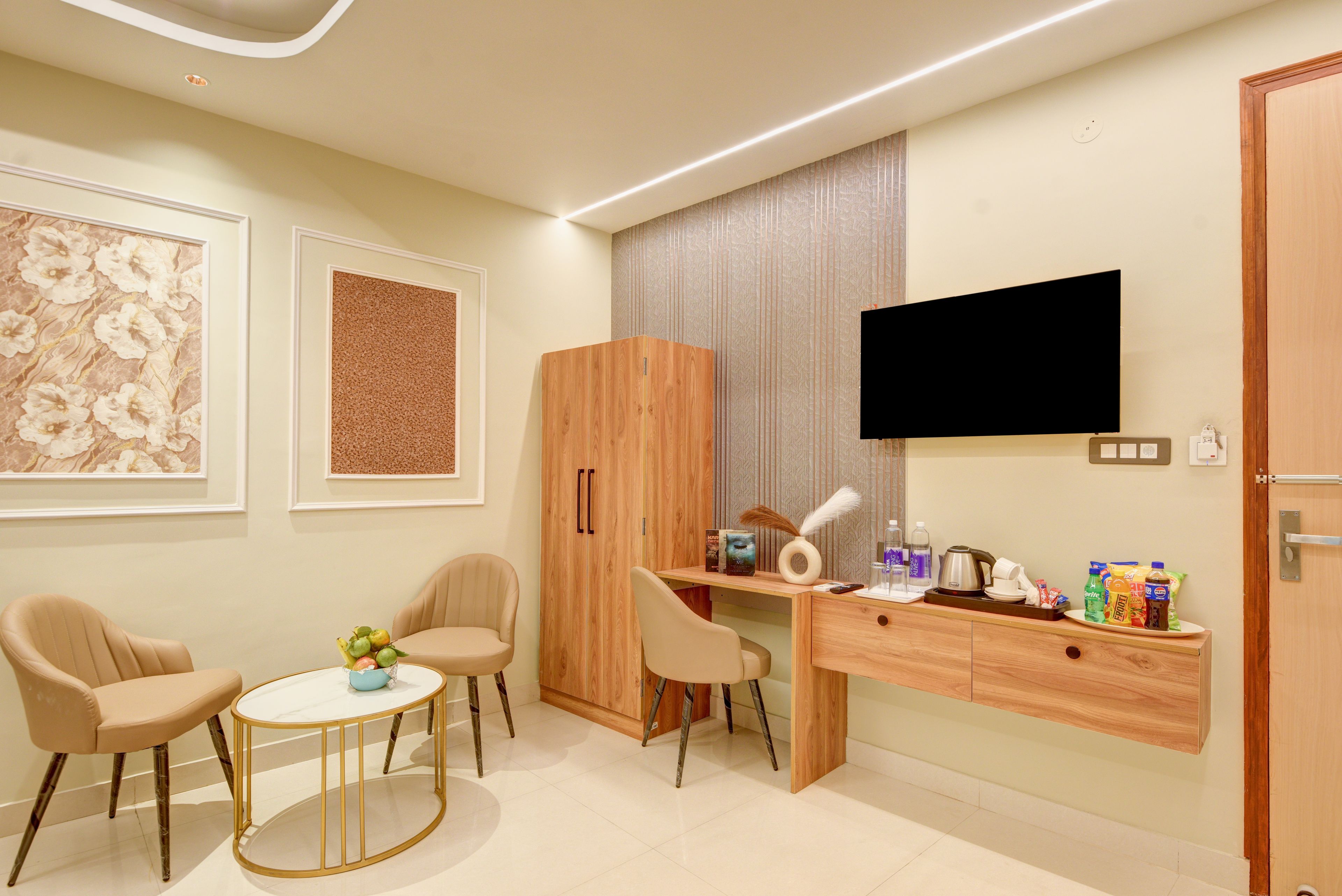 A modern hotel room with a wooden desk, two chairs, a television, and a minibar.