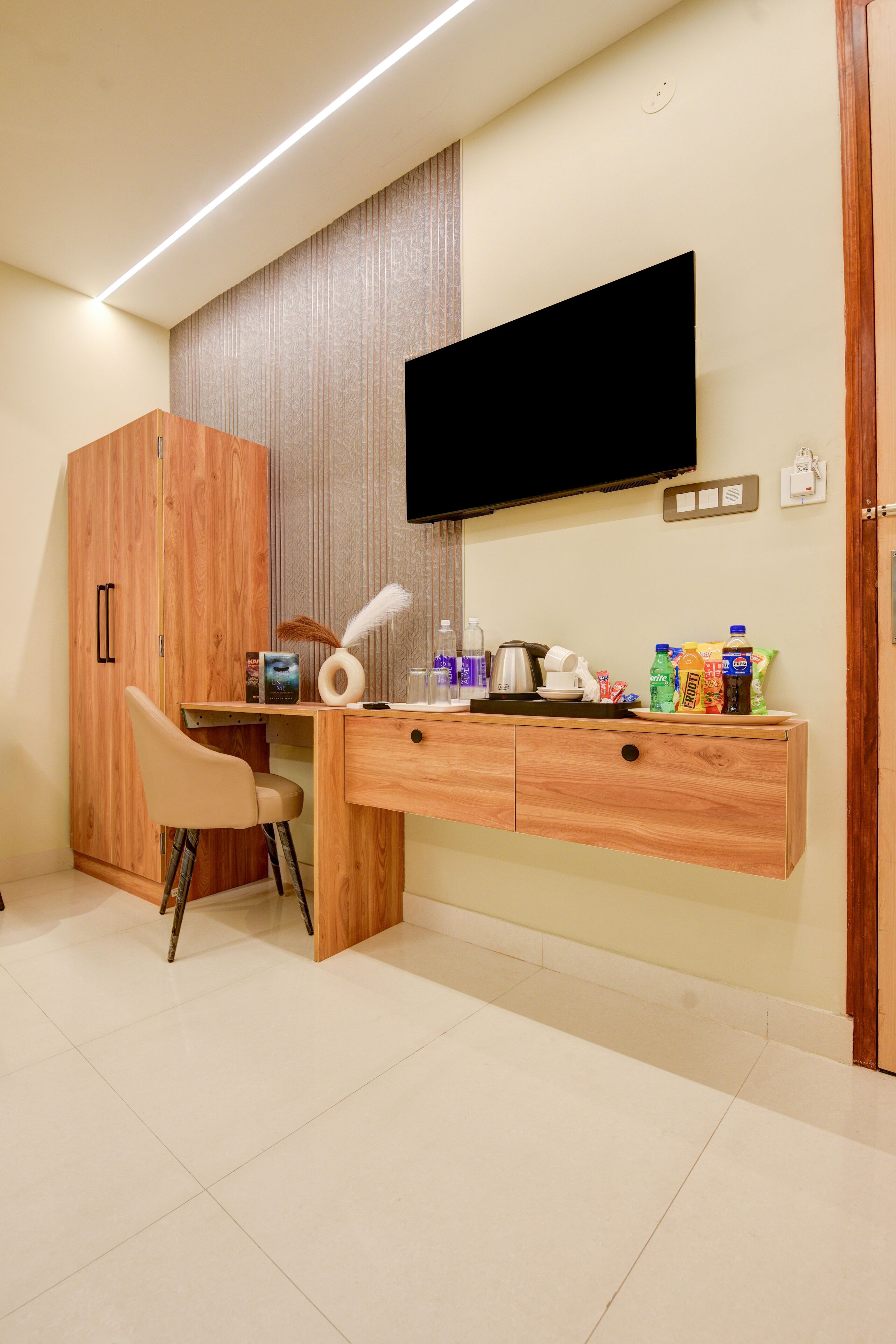 Une pièce comprenant un bureau en bois, une chaise, une armoire, un téléviseur fixé au mur et une petite étagère avec divers objets.