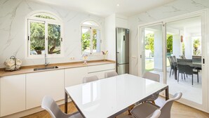 A modern kitchen with white marble countertops, a stainless steel refrigerator, and a dining area with a white table and chairs. - Luxury villa in the center of Marbella (Marbella)