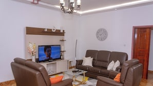 A modern living room with a sofa, two armchairs, a coffee table, a TV, and a clock on the wall. - Stuttgart Apartment at Résidence Baho Comfort, Elegance & Tranquility (Douala)