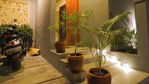 Ingresso moderno di un edificio, con una motocicletta parcheggiata, piante in vaso e una panchina in legno.