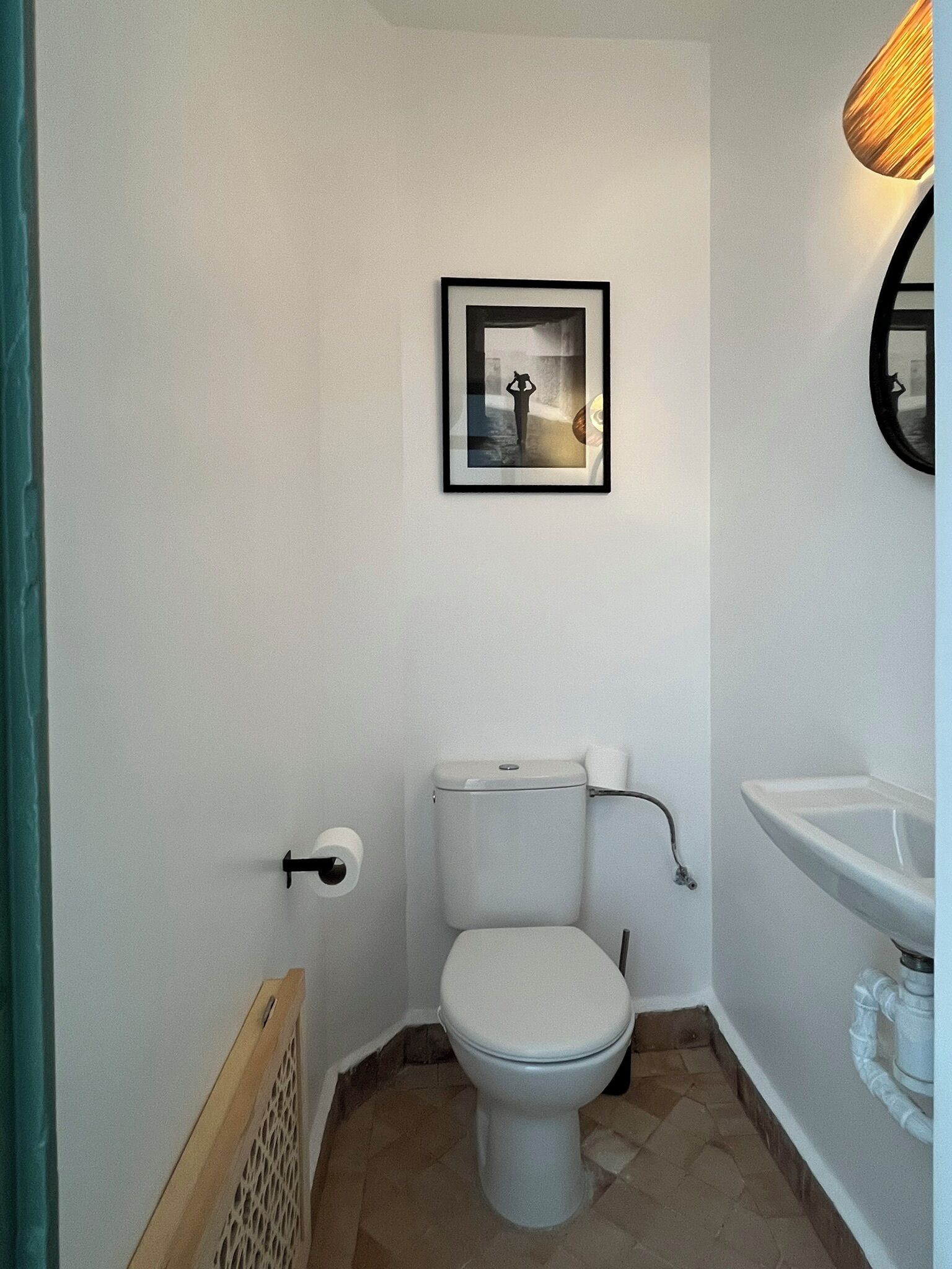 Un baño pequeño con inodoro, lavamanos, un cuadro en la pared y un espejo.