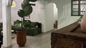 Uma sala ampla com uma grande planta em vaso, um baú de madeira e um sofá verde.