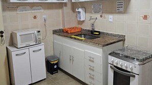 A compact kitchen with white cabinets, a microwave, a gas stove, and a sink. - Cabo Frio Seasonal Apartment - 3 minutes from the beach. Ideal for families (Vila Nova Cabo Frio)
