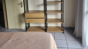 A bedroom with a bed, a wardrobe with shelves, and a door. - Cabo Frio Seasonal Apartment - 3 minutes from the beach. Ideal for families (Vila Nova Cabo Frio)
